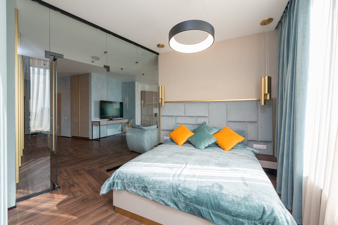 Soft comfortable bed with cushions in modern spacious bedroom with parquet floor and glass wall